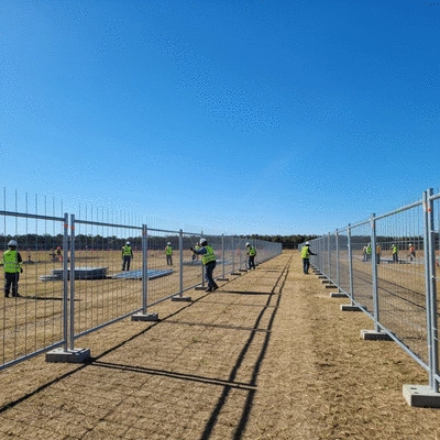 Temporary event fencing being set up in an open field, with construction workers in the background, clear sky, no text, no words, no typography, 8K