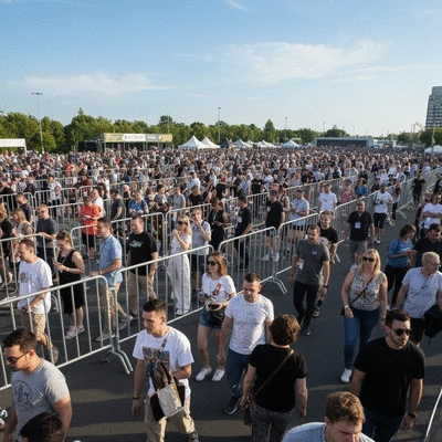 Crowd control barriers in use at an outdoor event, with people moving orderly, bright daylight, no text, no words, no typography, 8K